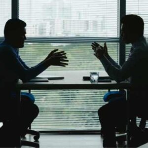 negocjacje-pandemia-699 Zdjęcie przedstawiające dwie negocjujące osoby po przeciwnych stronach biurka